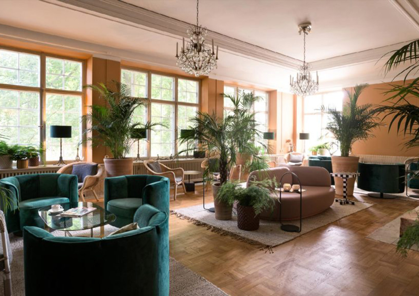 Ljus salong på Näsby Slott med kristallkronor, gröna sammetsfåtöljer och palmer
