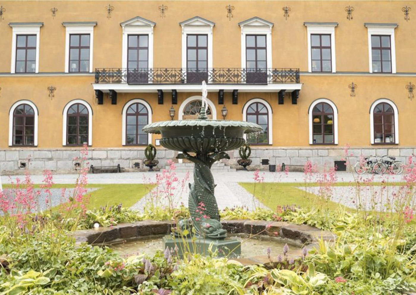 Ulfsunda Slotts gula fasad med fontän och blommande slottsträdgård i Bromma