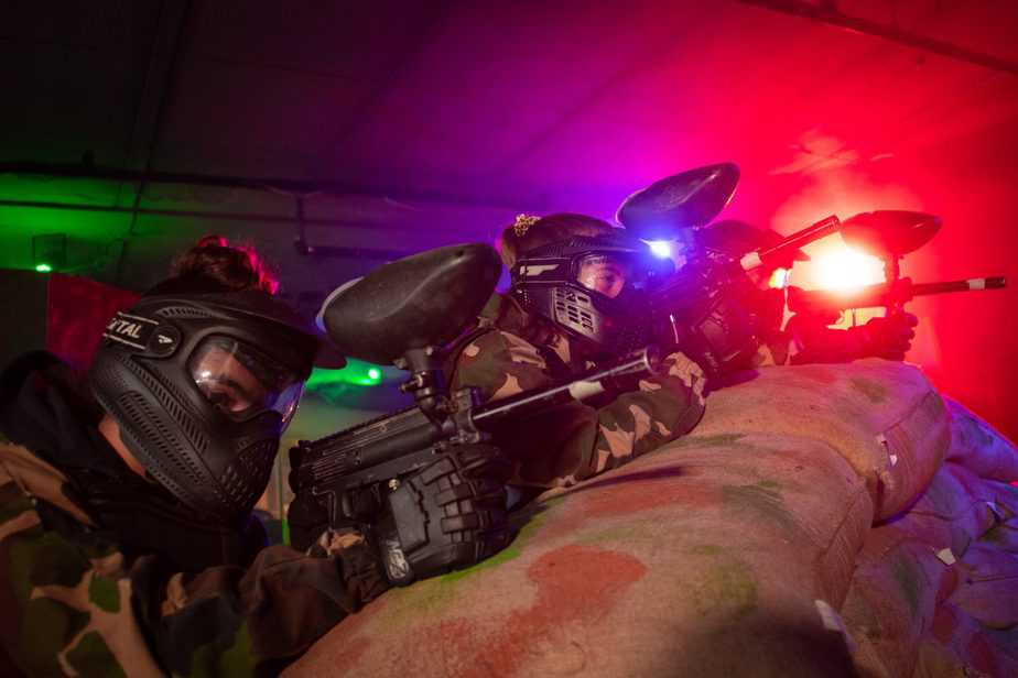 Barn med skyddsmasker och markörer spelar paintball i färgglad belysning